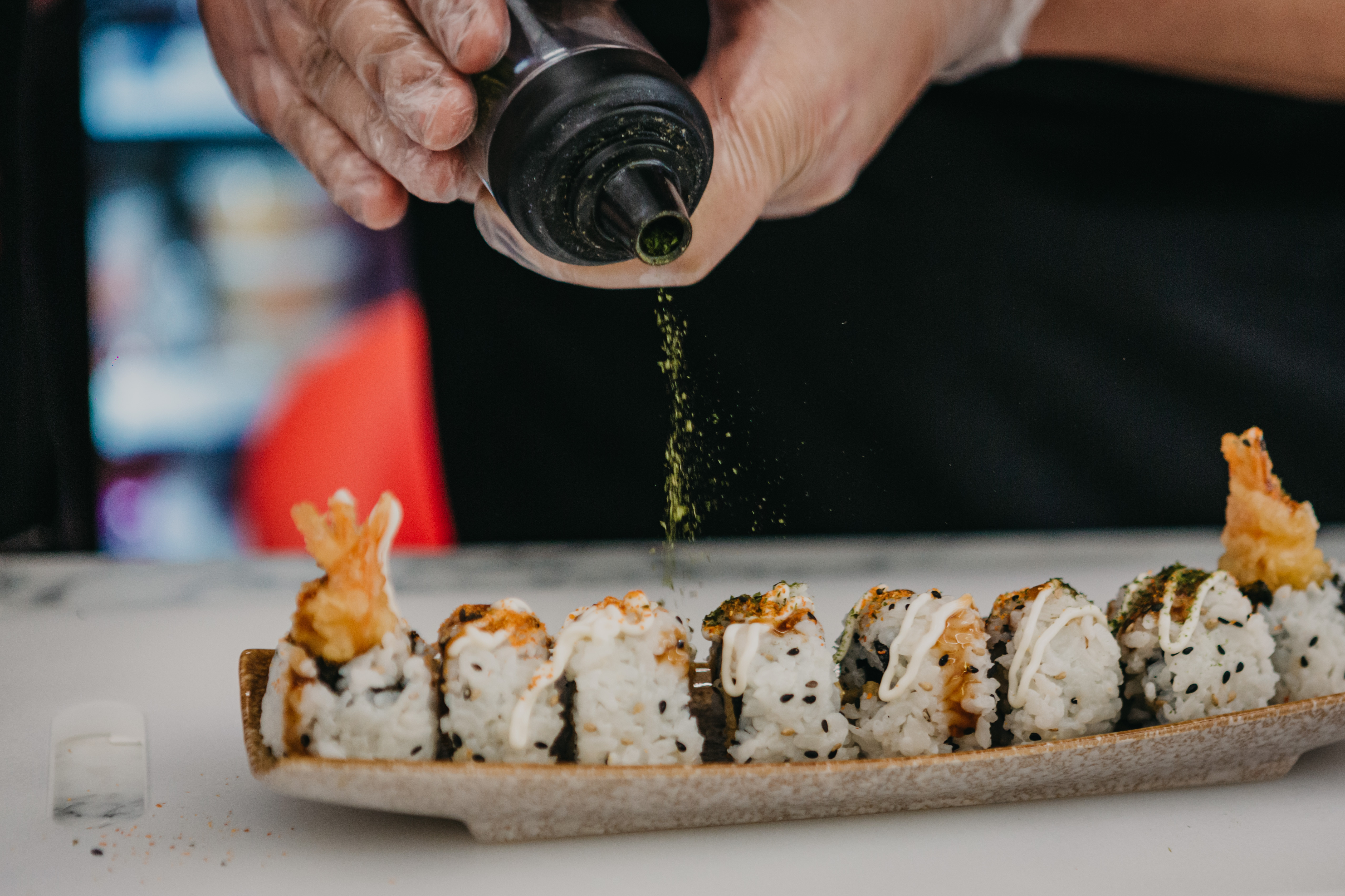 Close up of hands adding seasoning to a row of sushi rolls